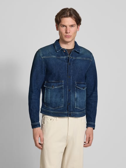 Männermodel trägt Jeansjacke mit Pattentaschen und Kentkragen von Replay in Dunkelblau aus Baumwoll-Mix mit Stretch-Anteil, Straight Fit, Druckknopfverschluss, Label-Detail; Ganzkörperansicht von vorne. Rückenlänge bei Größe M: 68 cm, Schulterbreite: 38 cm, Brustweite: 51 cm, Ärmellänge: 66 cm.