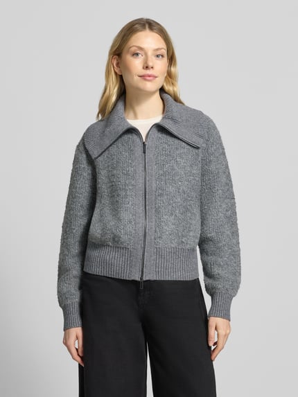Modelka nosi Regular Fit Strickjacke mit Zweiwege-Reißverschluss Modell 'Teski' od someday., szary, faktura dzianiny, długość pleców w rozmiarze 36: 52 cm, szerokość ramion w rozmiarze 36: 45 cm, szerokość klatki piersiowej w rozmiarze 36: 57 cm, długość rękawa w rozmiarze 36: 70 cm, widok całej sylwetki z przodu.
