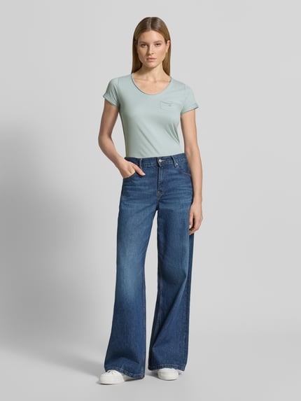 Frauenmodel trägt Damen T-Shirt mit V-Ausschnitt und Brusttasche, Modell 'GS23' von G.I.G.A. DX aus reiner Baumwolle, Regular-Fit, Rückenlänge bei Größe 36: 64 cm, pastellgrün, glatte Textur, kombiniert mit blauer Jeans, Ganzkörperansicht von vorne.