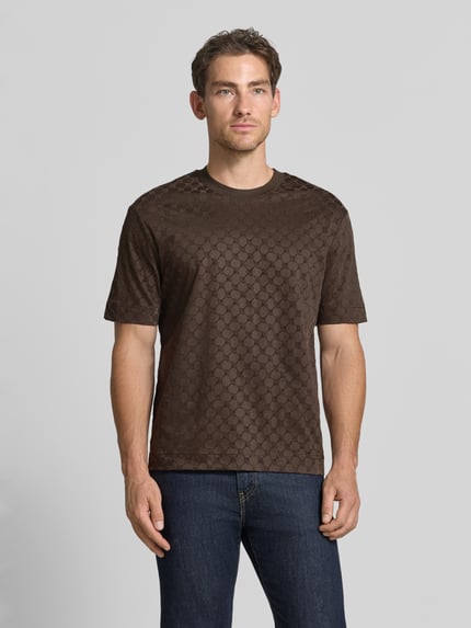 Männermodel trägt Regular Fit T-Shirt aus reiner Baumwolle Modell 'Varo' von JOOP! COLLECTION in Dunkelbraun mit dezentem Muster, Ganzkörperansicht von vorne.