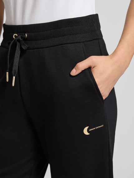 Kobiecy model nosi Sweatpants mit elastischem Bund od ARMANI EXCHANGE, czarny kolor, bawełniany miks, luźny krój, kieszenie, zbliżenie na biodra.