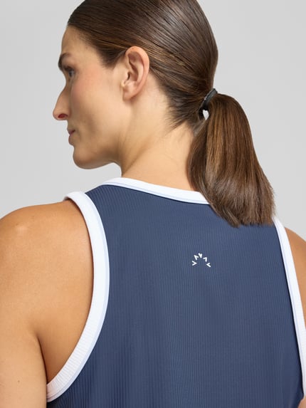 Frauenmodel trägt Top mit Rundhalsausschnitt Modell 'Tegan' von VARLEY in Dunkelblau mit weißen Rändern, elastischer Material-Mix, taillierte Passform, Rückenlänge bei Größe S 62 cm, Nahaufnahme Rückansicht.