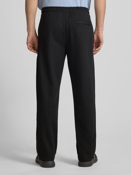 Męski model nosi Regular Fit Sweatpants aus Baumwoll-Mix Modell 'DAVROPANT' od HUGO, czarne, prążkowane, z naszywką logo, widok całej sylwetki z tyłu.