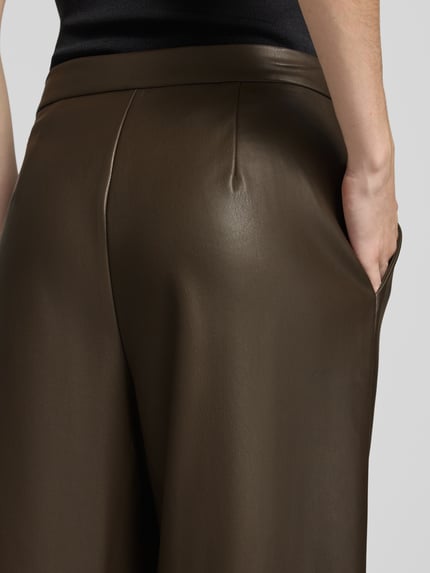 Frauenmodel trägt Regular Fit Lederhose mit Bundfalten von STEFANEL in einfarbiger Lederoptik, Teilungsnähte, Nahaufnahme Rückansicht.