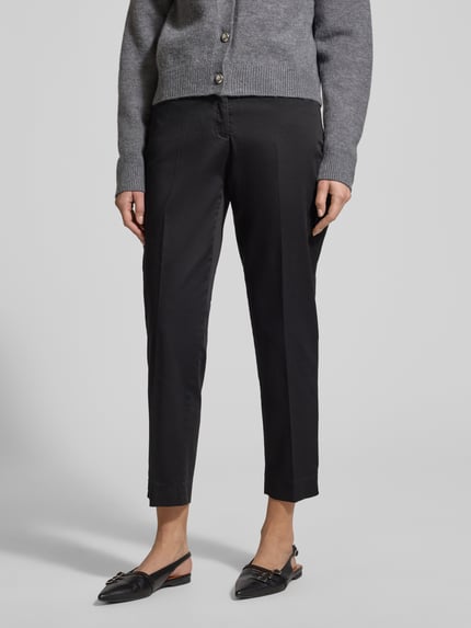 Frauenmodel trägt Straight Fit Stoffhose mit Lyocell-Anteil Modell 'Mara' von BRAX in Schwarz, Damen Stoffhose, Bügelfalten, verkürzte Passform, elastischer Baumwoll-Lyocell-Mix, Eingriff- und Gesäßtaschen, Knopf- und Reißverschluss, Ganzkörperansicht von vorne.