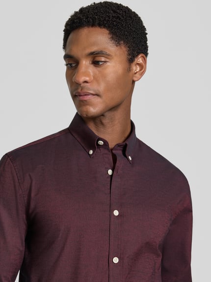 Männermodel trägt Regular Fit Freizeithemd aus Baumwoll-Mix Modell 'Oxford' von Lindbergh in Dunkelrot, Nahaufnahme Oberkörper. Baumwoll-Elasthan-Mix, Button-Down-Kragen, 1-Knopf-Manschetten, abgerundeter Saum.
