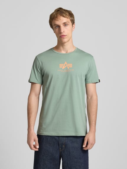Männermodel trägt T-Shirt mit Logo und Rundhalsausschnitt von Alpha Industries in Grün, Reine Baumwolle, Regular-Fit, Logo, Rückenlänge 67 cm, Ganzkörperansicht von vorne.