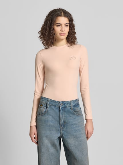 Frauenmodel trägt Slim Fit Longsleeve mit Logo-Detail von ANOTHER COTTON LAB in Beige, elastischer Baumwoll-Mix, Ganzkörperansicht von vorne.