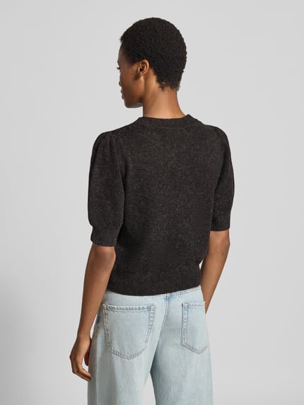 Frauenmodel trägt Regular Fit Pullover mit Puffärmeln von VERO MODA in Dunkelgrau zu heller Jeans, Textur grobstrick, Ganzkörperansicht Rückansicht.