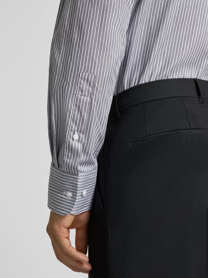 Männermodel trägt Regular Fit Business-Hemd aus Baumwolle von Christian Berg Men mit feinen weißen Streifen, Nahaufnahme Ärmel, Kontext: Herren Business-Hemd, reine Baumwolle, Regular Fit, langärmliges Design, Haifischkragen, Rückenlänge 82 cm, Schulterbreite 42 cm, Ärmellänge 65 cm.
