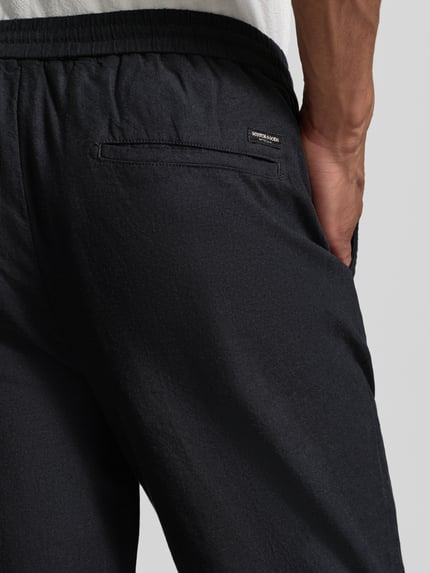 Mannenmodel draagt Jogpants aus Baumwoll-Leinen-Mix mit elastischem Bund van Scotch & Soda, regular fit, zwarte stoftextuur, detailopname rug.