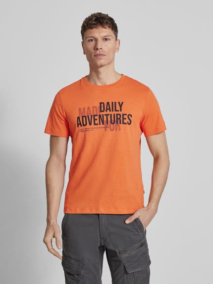 Männermodel trägt Regular Fit T-Shirt aus reiner Baumwolle von camel active, Herren T-Shirt mit Statement-Print in Orange, Rundhalsausschnitt, Rückenlänge 68 cm bei Größe M, Ganzkörperansicht von vorne.
