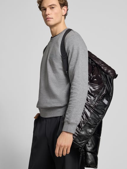 Männermodel trägt Regular Fit Steppjacke mit Logo-Patch Modell 'Coen' von khujo in glänzender Stepp-Optik, seitliche Nahaufnahme Oberkörper.