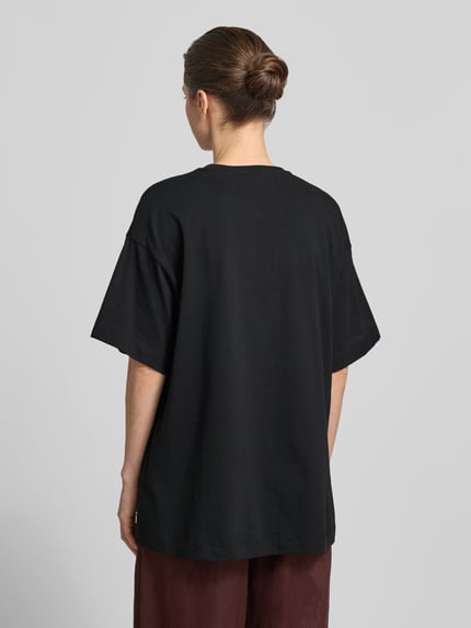 Kobiece model prezentuje damski t-shirt Oversized T-Shirt aus reiner Baumwolle Modell 'LILIE' od Vero Moda, jednokolorowy, krój oversized, z nadrukiem z motywem, krótki rękaw, wykonany z czystej bawełny, widok całej sylwetki z tyłu.
