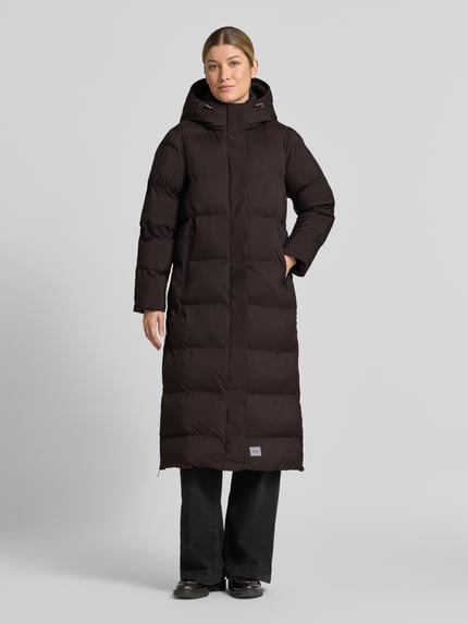 Frauenmodel trägt Steppmantel mit Reißverschlusstaschen Modell 'MAYLA4' von khujo in Dunkelbraun, strukturierte Steppoptik, Ganzkörperansicht von vorne. Rückenlänge 114 cm, Regular Fit, verdeckter Reißverschluss, Kapuze, Label-Detail.