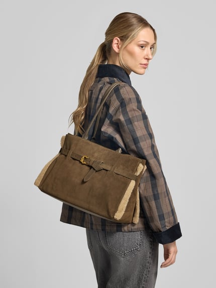 Frauenmodel trägt Handtasche aus echtem Leder Modell 'Sabine' von Coccinelle in Braun, rechteckige Form, Textur mit sichtbaren Nähten, Detailaufnahme Rückansicht. Hauptfach mit Druckknopfverschluss, Schulterriemen, Breite 36 cm, Länge 25 cm, Tiefe 15 cm, Riemenlänge 60 cm.