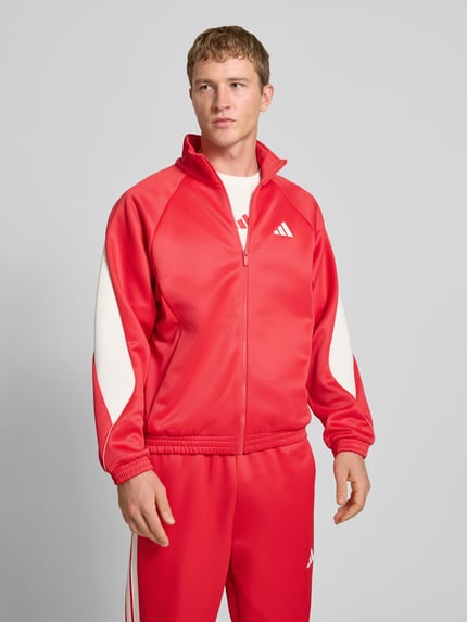 Männermodel trägt Trainingsjacke mit Stehkragen und Logo von adidas Sportswear in Rot mit weißen Details, Regular Fit, Nahaufnahme Oberkörper.