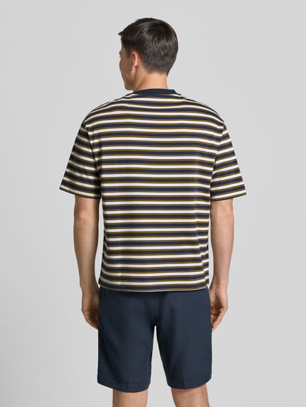 Mannenmodel draagt Relaxed fit T-shirt uit pure katoen model 'ASPEN 2' van SELECTED HOMME met beige, blauwe en zwarte strepen. Ganzlichaamsaanzicht achteraan.