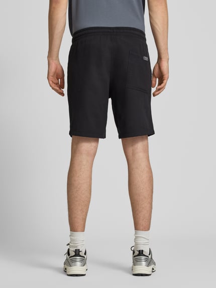 Mannenmodel draagt Shorts met structuurpatroon model 'JAIDEN' van Jack & Jones, puur katoen, regular fit, elastische band, tunnelkoord, kleur zwart, zichtbare achterzak, context: heren korte broek van puur katoen, regular fit, structuurpatroon, elastische band met tunnelkoord, bandwijdte maat M 43 cm, binnenbeenlengte 23 cm, volledige achteraanzicht