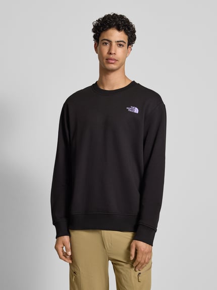 Männermodel draagt Sweatshirt mit Label-Print van The North Face, zwart, puur katoen, relaxed fit, ribboorden, ronde hals, labelprint. Ganzkörperansicht van voren.