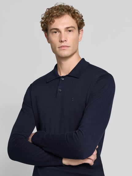 Männermodel trägt dunkelblaues Slim Fit Poloshirt aus reiner Baumwolle von ARMEDANGELS, glatte Oberfläche, Nahaufnahme Oberkörper.