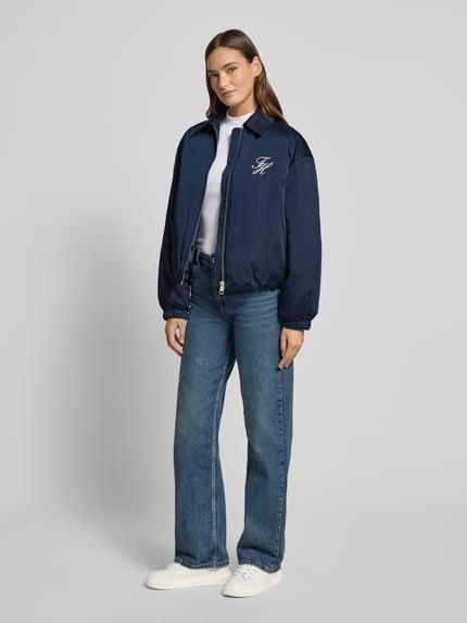 Modelka kobieca nosi Regular Fit Bomberjacke mit Logo-Detail od Tommy Hilfiger, granatowy odcień, gładka faktura, długie rękawy, elastyczne wykończenia, widok całej sylwetki z przodu.