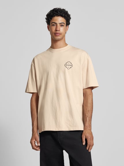 Męski model nosi Oversized T-Shirt mit Label-Print Modell 'Paide' od Pegador z bawełny, okrągły dekolt, jasny beż, nadruk z logo, całkowita długość tyłu 70 cm przy rozmiarze M, krój oversized, widok z przodu całej sylwetki.