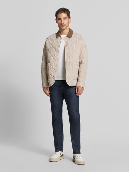 Männermodel trägt Steppjacke mit Eingrifftaschen von CINQUE in Beige, gerader Schnitt, kontrastierender Kragen, Ganzkörperansicht von vorne.