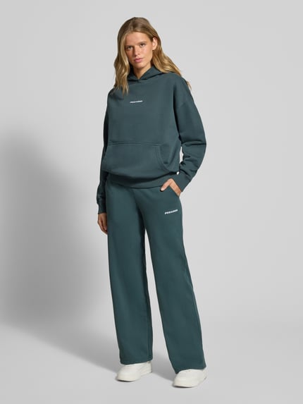 Kobiece model prezentuje Flared Fit Jogginghose aus Baumwoll-Mix Modell 'Anni' von PEGADOR, zielony kolor, wpuszczane kieszenie, wyhaftowane logo, elastyczny pas, długość wewnętrzna nogawki w rozmiarze S: 82 cm, Ganzkörperansicht von vorne.
