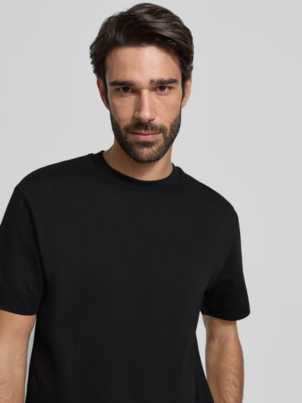 Männermodel trägt T-Shirt mit Label-Detail Modell 'Achilleas' von JOOP! Collection aus reiner Baumwolle, Regular-Fit, Nahaufnahme Oberkörper.