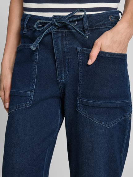 Frauenmodel trägt Barrel Jeans aus Baumwoll-Mix von Buena Vista in Dunkelblau mit großen Fronttaschen und Bindegürtel, Nahaufnahme Oberkörper. Damen Barrel Jeans von Buena Vista.