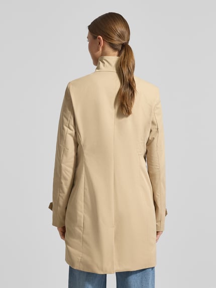 Vrouwenmodel draagt 'Trenchcoat mit Stehkragen und Ärmelriegeln' van Christian Berg Woman Selection in beige, a-lijn, detailsteek, knoopsluiting, staande kraag, mouwriem, ruglengte 84 cm, schouderbreedte 39 cm, borstwijdte 47 cm, mouwlengte 63 cm, geheel achteraanzicht.