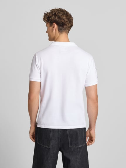 Männermodel trägt Regular Fit Poloshirt mit Label-Patches von Superdry aus Reine Baumwolle, weiße Farbe, Rückenlänge 68 cm, Ganzkörperansicht Rückansicht.