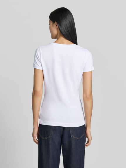 Frauenmodel trägt T-Shirt mit Logo und Rundhalsausschnitt von Guess im Slim Fit aus Baumwoll-Elasthan-Mix in Weiß, Ganzkörperansicht Rückansicht.