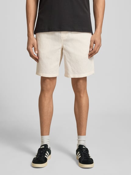 Mężczyzna nosi Shorts mit Strukturmuster Modell 'JAIDEN' von Jack & Jones w kolorze ecru, krój regular fit, materiał bawełniany, Szerokość w rozmiarze M: 41 cm, długość nogawki: 21 cm, tekstura strukturalna, Ganzkörperansicht von vorne.
