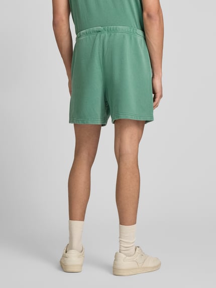 Männermodel trägt Sweatshorts mit Eingrifftaschen von CHAMPION in Grün, Baumwoll-Mix, Regular Fit, elastischer Bund, Ganzkörperansicht Rückansicht.