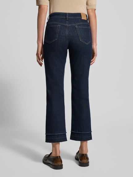 Frauenmodel trägt Feminine Fit Jeans in verkürzter Passform von Marc Cain, dunkler Baumwoll-Elasthan-Mix, Eingrifftaschen, Ganzkörperansicht Rückansicht.