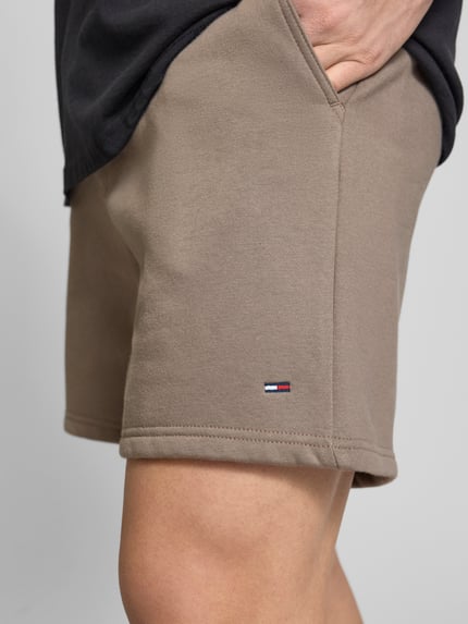 Männermodel trägt Regular Fit Shorts aus Baumwoll-Mix von Tommy Jeans in Beige mit Logo-Detail, Sweat-Textur, Nahaufnahme Oberschenkel.
