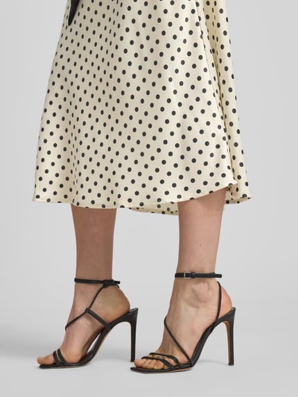 Vrouwenmodel draagt Midirock met seitlichem Reißverschluss Modell 'PELLA' van YAS in beige met zwarte stippen, straight fit, stretchmateriaal, detailopname onderlichaam.
