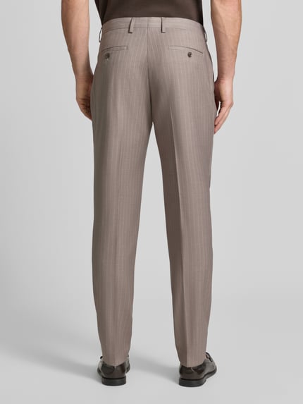Männermodel trägt Anzughose mit Bügelfalten von MCNEAL in Beige mit feinem Streifenmuster, Gesäßtaschen, Ganzkörperansicht Rückansicht.
