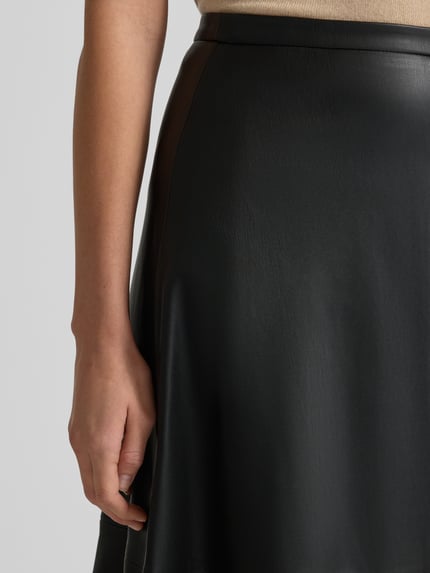 Frauenmodel trägt Midirock in Leder-Optik Modell 'PARIS' von Mango, schwarzer Look, lockerer Schnitt, Nahaufnahme Oberkörper. Bundweite 37 cm, Gesamtlänge 83 cm bei Größe 36, Nahtreißverschluss.