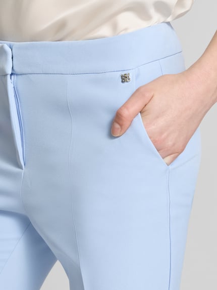 Frauenmodel trägt Slim Fit Hose mit Bügelfalten Modell 'HAGONIA-1' von HUGO in Hellblau, unifarben, mit Logo-Applikation und Eingrifftaschen, Nahaufnahme Oberkörper.
