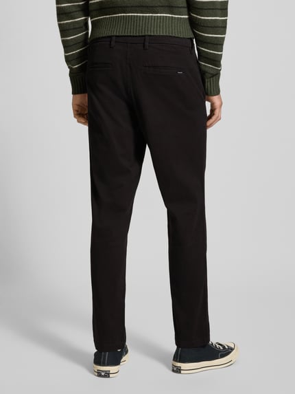 Mężczyznamodel nosi czarną Straight Fit Chino mit Gesäßtaschen Modell 'Stollie' von Jack & Jones z elastycznej bawełnianej mieszanki, tylne kieszenie, kieszenie boczne, zapięcie na guzik i zamek, szerokość w rozmiarze 32/32: 44 cm, długość nogawki wewnętrznej w rozmiarze 32/32: 75 cm, widok całej sylwetki z tyłu.