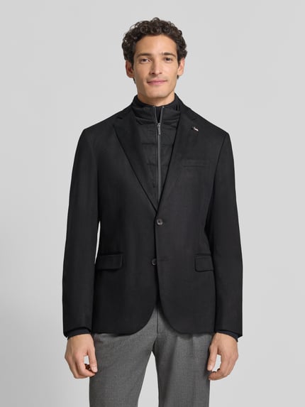 Męski model nosi Regular Fit Sakko aus elastischem Material-Mix mit Label-Detail od bugatti, kolor czarny, zamek błyskawiczny, stójka, marynarka na 2 guziki, kieszeń na piersi, kieszenie z patką, długość tyłu 74 cm, szerokość w rozmiarze 50: 43 cm, długość rękawów 66 cm, kołnierz z połami, Ganzkörperansicht von vorne.