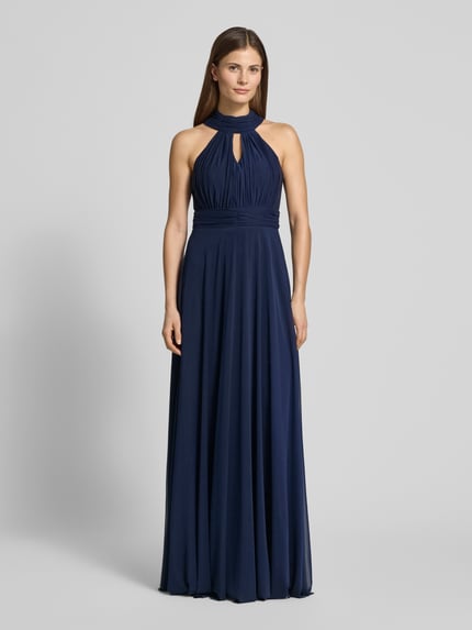 Frauenmodel trägt Abendkleid mit rückseitiger Schnürung von TROYDEN COLLECTION, dunkelblauer Chiffon, tailliert, Maxikleid, Ganzkörperansicht von vorne.