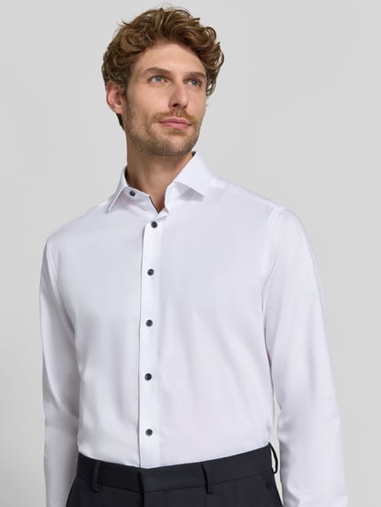Männermodel trägt Modern Fit Businesshemd mit extra langem Arm von OLYMP in Weiß mit dunklen Knöpfen, Nahaufnahme Oberkörper, Herren Businesshemd von OLYMP.