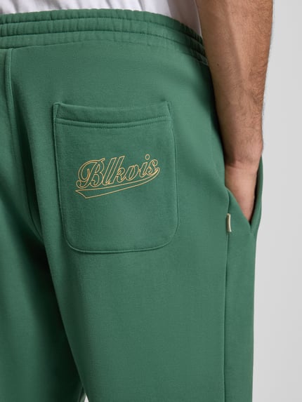 Männermodel trägt Regular Fit Sweatpants mit Gesäßtasche Modell 'Source' von BLKVIS in Grün aus reiner Baumwolle, Detailaufnahme Rückansicht.