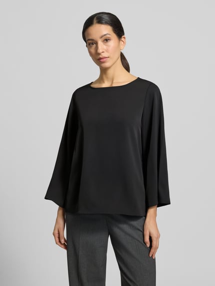 Modelka kobieca ma na sobie Blusenshirt mit Rundhalsausschnitt od comma, czarny, luźny krój, materiał z domieszką stretchu, długość tyłu 59 cm, długość rękawa 52 cm, ujęcie całej sylwetki z przodu.