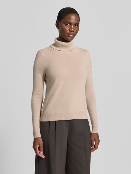 Frauenmodel trägt Regular Fit Rollkragenpullover aus reinem Kaschmir von Christian Berg Woman in Beige, gerippte Abschlüsse, Ganzkörperansicht von vorne.