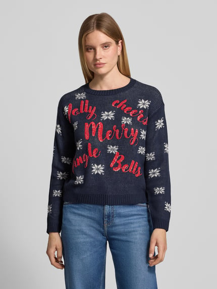 Frauenmodel trägt Pullover mit Pailletten-Schriftzug von VERO MODA, mehrfarbig, Sternenmuster, Strick, Regular Fit, Nahaufnahme Oberkörper.